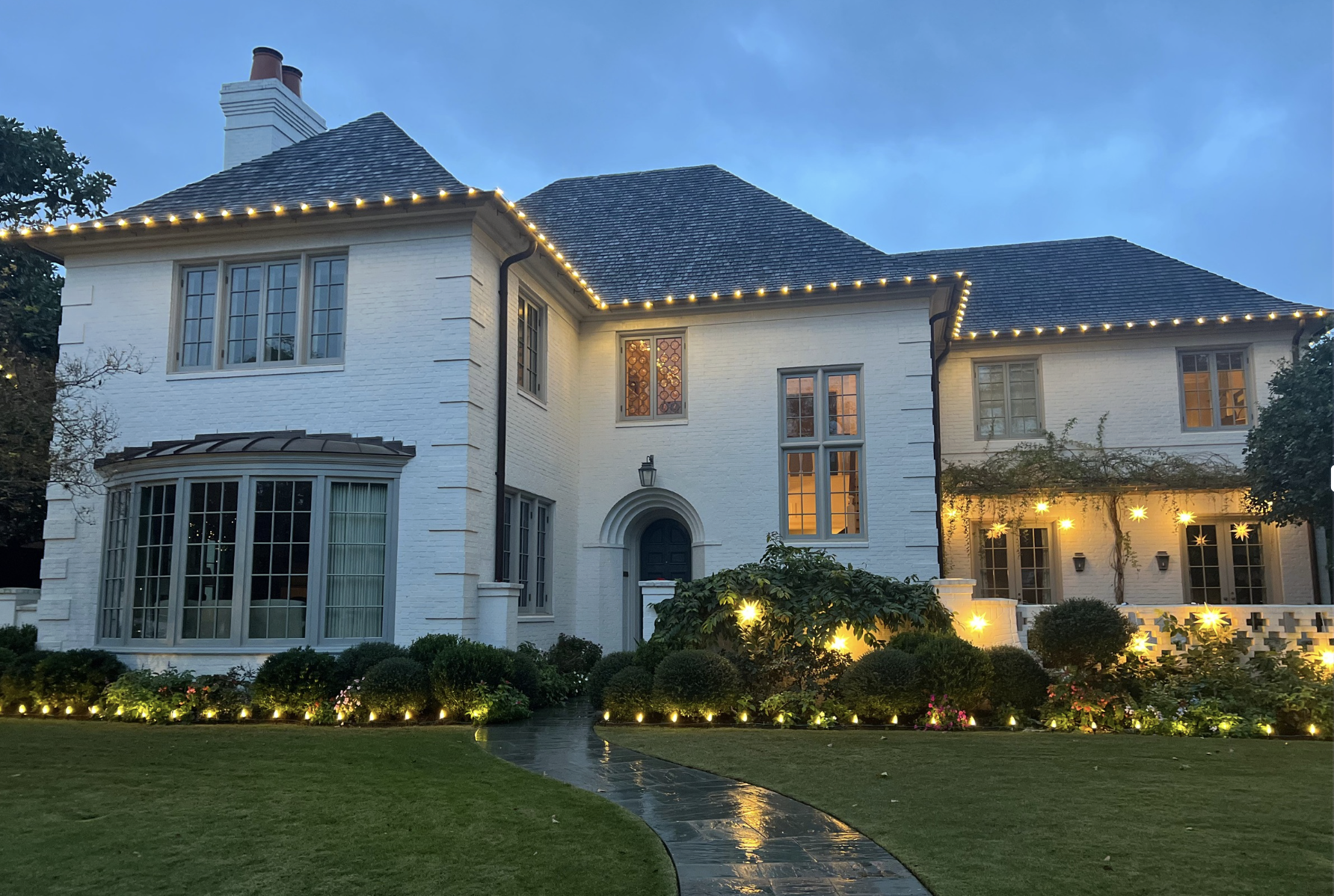 Elegant white brick home with professional Christmas lights along rooflines and landscape lighting